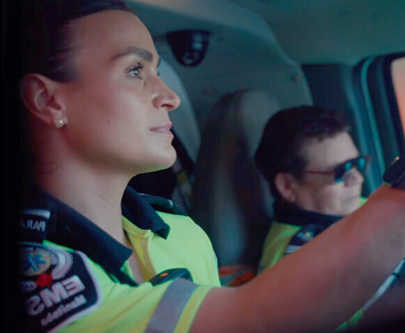 Danielle driving an ambulance with her partner in the background.